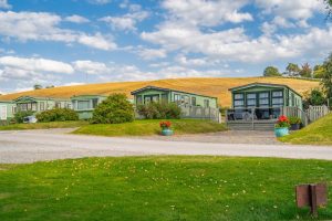 Row of green static holiday homes set against a backdrop of rolling Lake District hills.