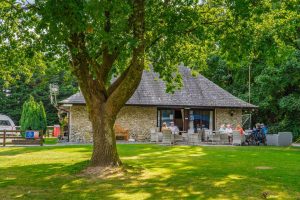 Traditional stone-built clubhouse with guests enjoying outdoor seating under a mature tree.